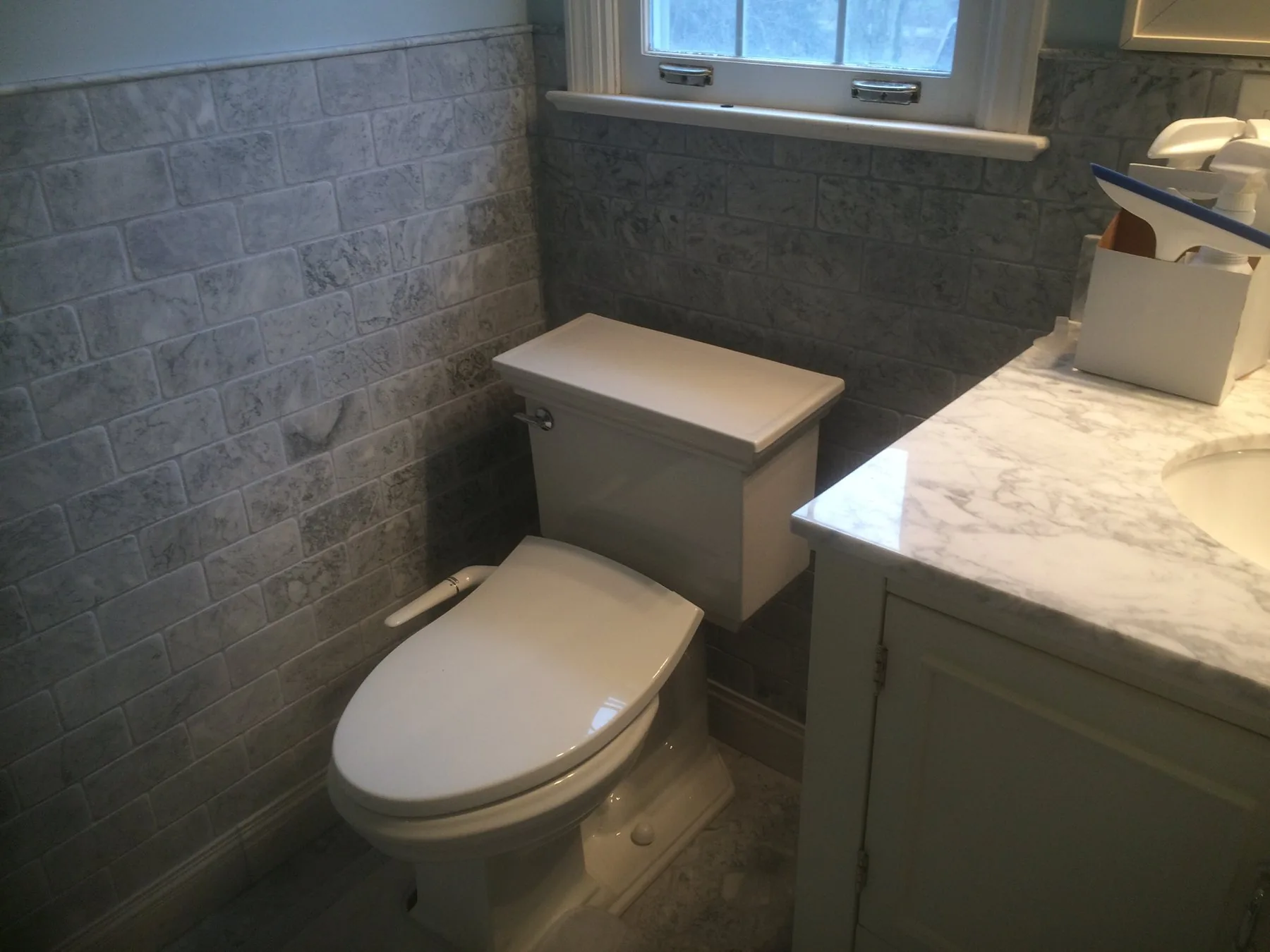 Bathroom remodeled by Edward Construction with a stone-look tile wall, marble counter, and gray vanity