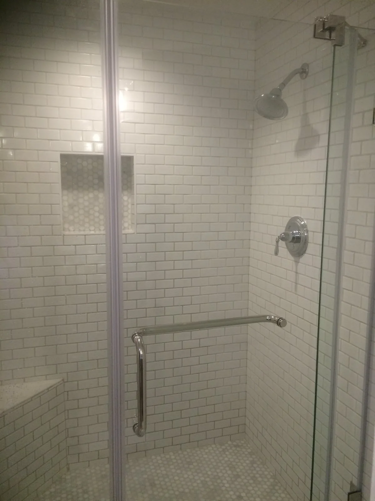 White subway tile shower with a glass door and mosaic floor