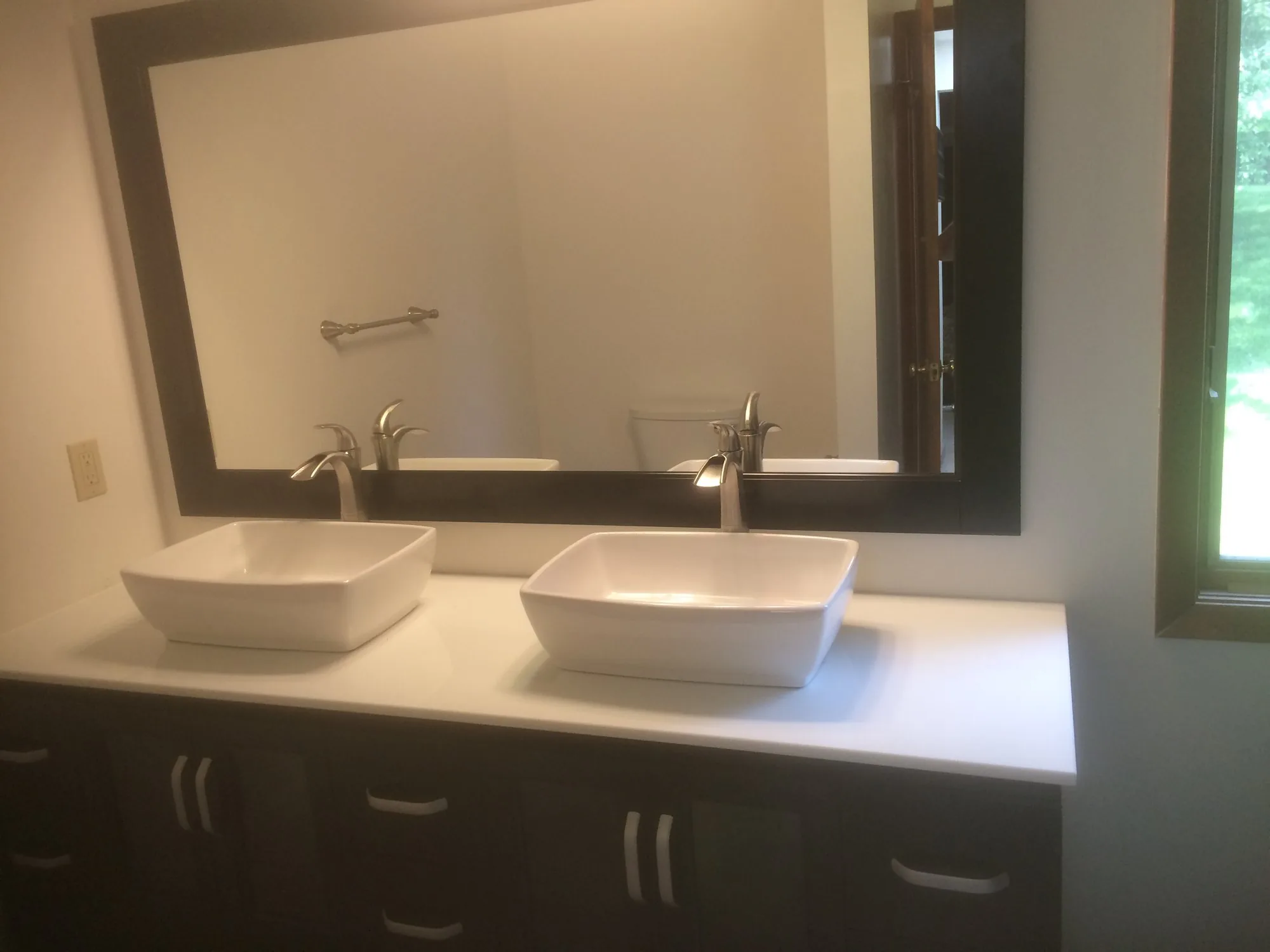 Finished bathroom by Edward Construction with two vessel sinks on a dark vanity and a framed mirror