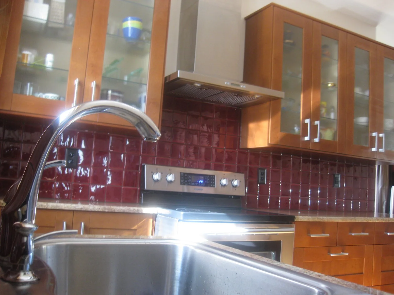 Kitchen by Edward Construction with a red glass backsplash and glass front upper cabinets