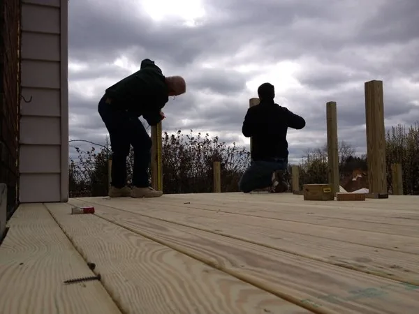 Two people setting railing posts on a newly boarded deck at dusk