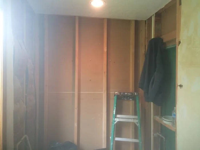 Bathroom stripped back to bare studs with plastic sheeting and a ladder